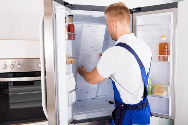 Professional young repairman in worker uniform and cap with modern toolbox with equipment is repairing of refrigerator on the kitchen