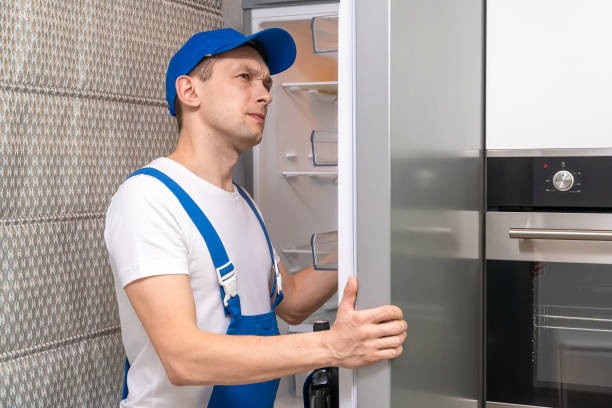 Uniformed repairman repairs the refrigerator door in the kitchen